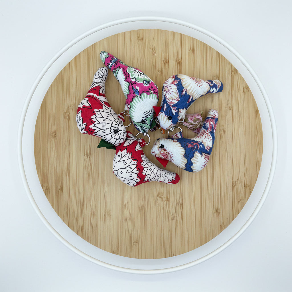 Three small fabric-covered golf tees with floral prints in red, blue, white, and pink, arranged on a round bamboo tray.